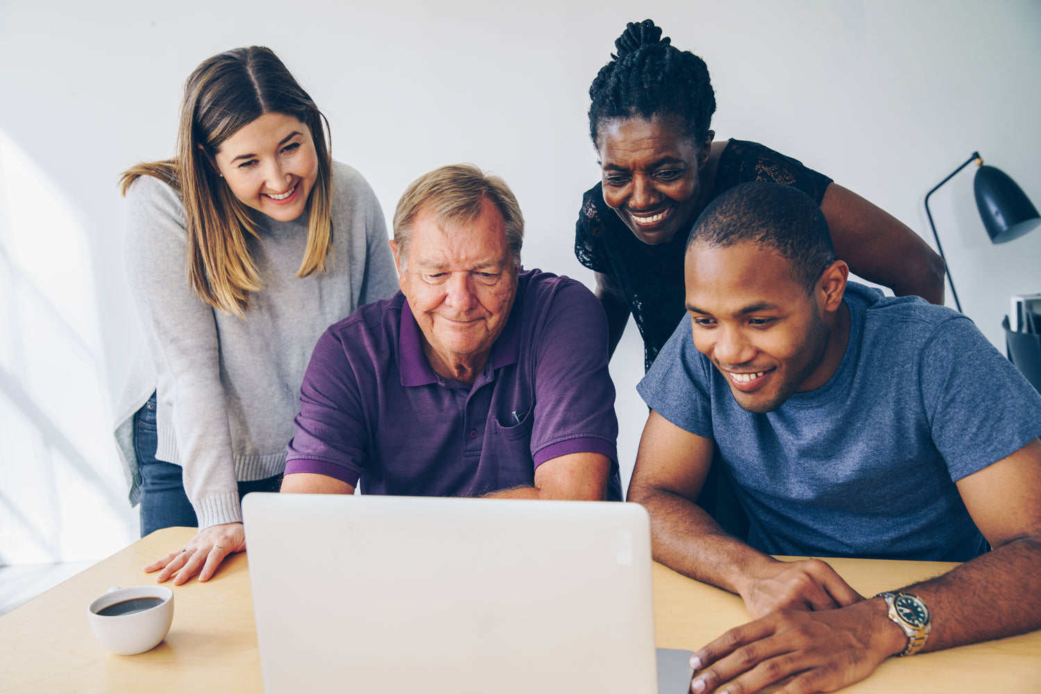 Four people smiling as they look at a computer. 